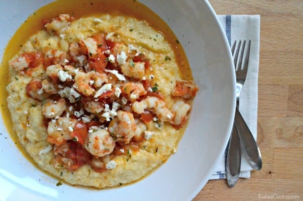 Top view of a white bowl filled with grits and shrimp on top with sauce on a wood countertop.