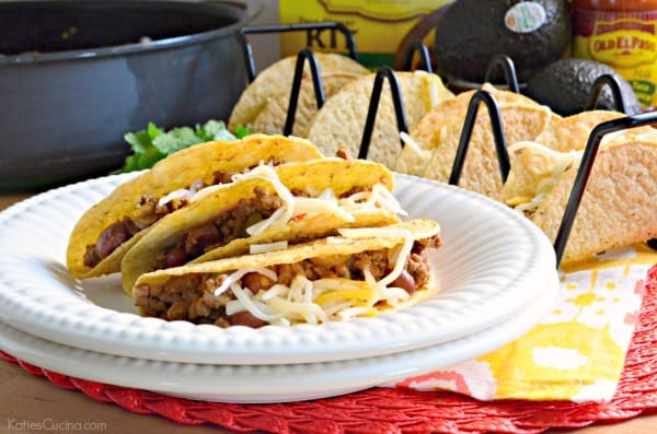 Tacos stacked on two white plates filled with meat and cheese.