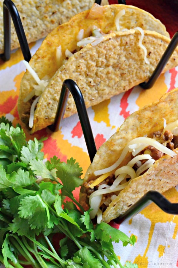 Taco rack holding crunchy tacos stuffed with ground beef, beans, and cheese.