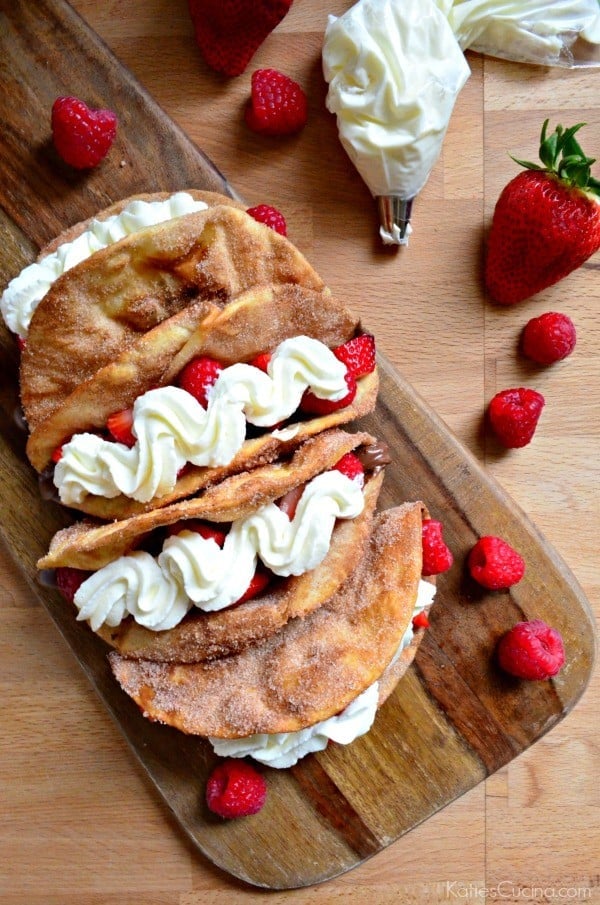 Top view of a board filled with dessert tacos with fruit and whipped cream.