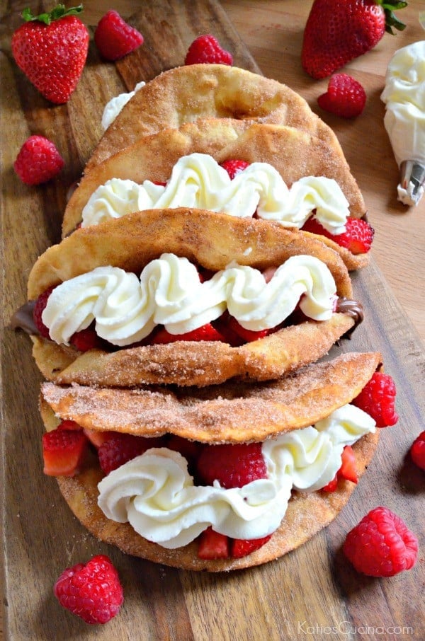 Four dessert tacos filled with strawberries and raspberries with whipped cream.