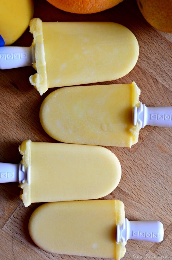 Top view of four orange popsicles staggered on wood countertop. 