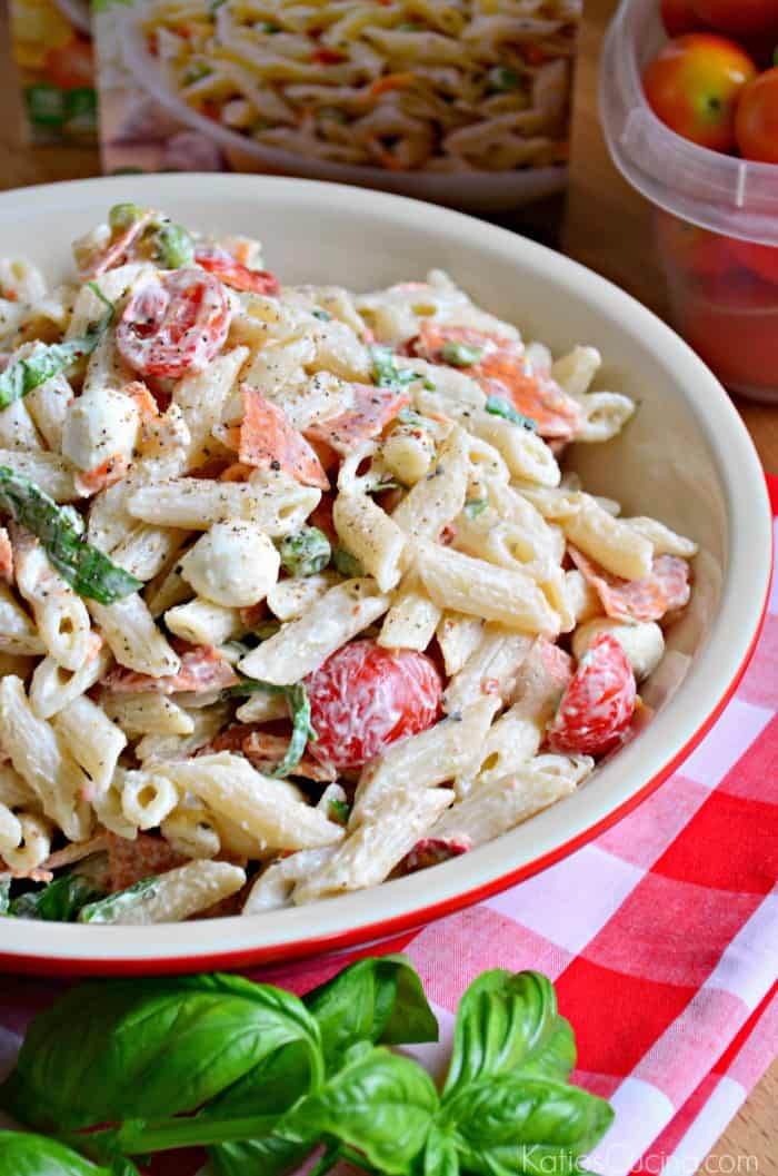 Close up of penne creamy pasta salad with tomatoes and basil in a red dish.