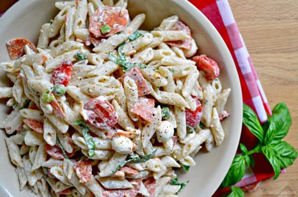 Top view of creamy tubed pasta salad with sliced grape tomatoes, basil, and chopped pepperoni.