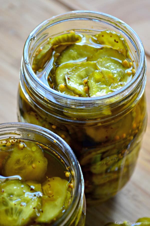 Two jars filled with Bread and Butter Pickles in glass mason jars on a wood countertop.