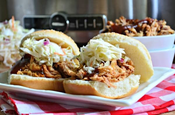 Two sandwiches filled with pulled chicken, barbecue sauce and coleslaw on a white platter. 