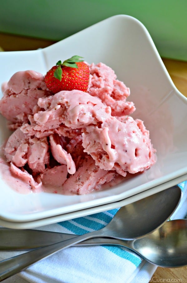 White square/curved bowl filled with strawberry ice cream with a fresh strawberry on top.