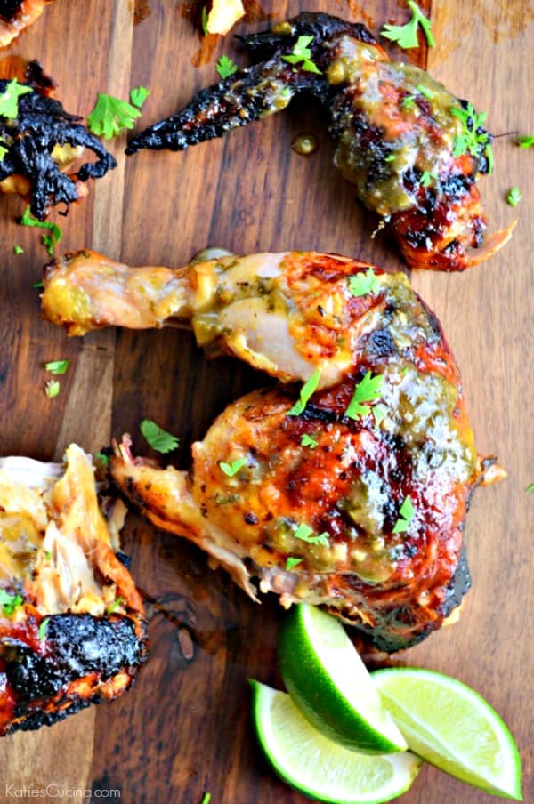 Grilled chicken thigh and leg on a wood cutting board with three lime wedges next to it.