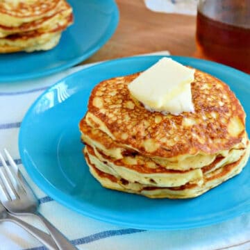 Blue plate with three pancakes stacked with butter on top.