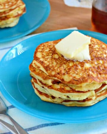 Blue plate with three pancakes stacked with butter on top.