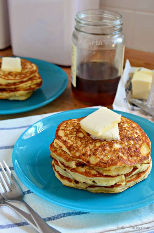 Blue plate with pancakes stacked on top of each other with butter and syrup.