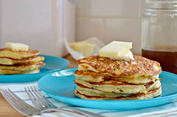 Blue plate with 5 pancakes stacked on top of each other with two square pieces of butter on top.