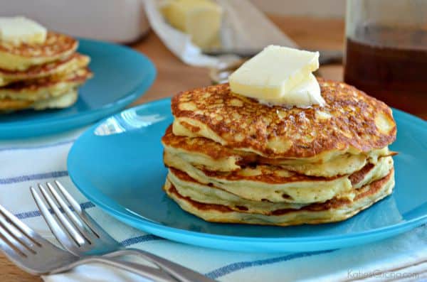 Five pancakes stacked on top of a bright blue plate with two forks next to the plate.