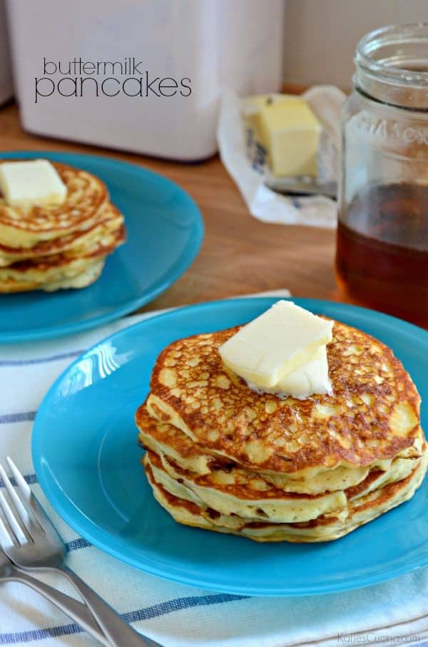 A stack of buttermilk pancakes with a square of butter on top with syrup in the background.