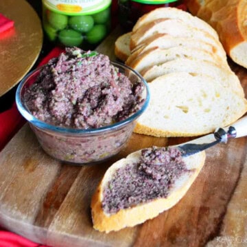 Bowl of brown olive spread with baguettes and spread on one slice.