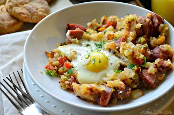 plated potatoes, kielbasa, and over easy eggs next to biscuits and two forks.