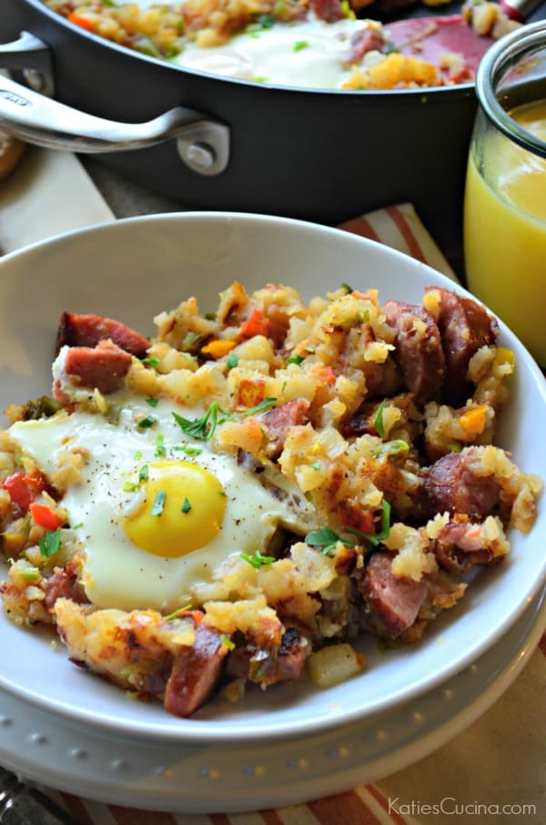 Kielbasa Breakfast Skillet in a bowl with an over-easy egg next to skillet filled with remaining food.