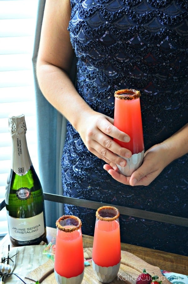 Female in blue dress holding a long stemmed glass filled with a pink drink.