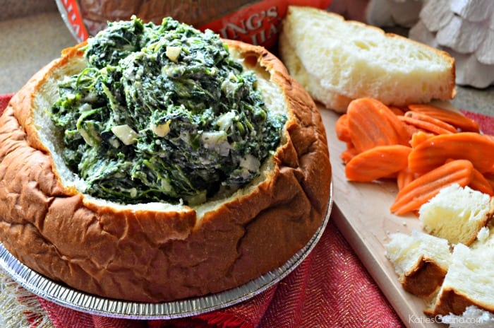 Bread bowl filled with spinach dip with bread and veggies next to it.