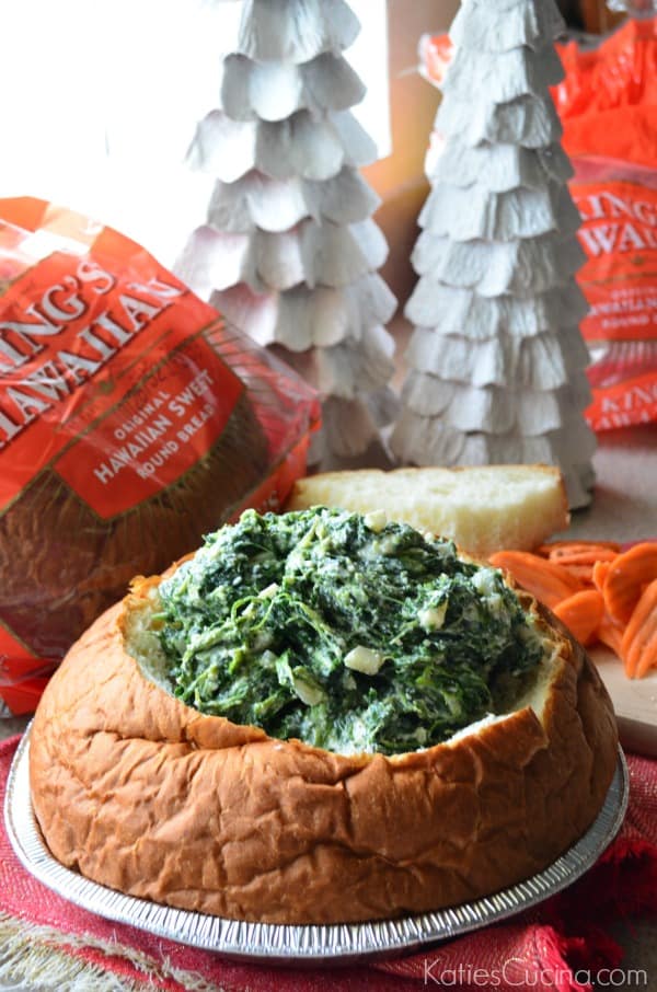 Bread bowl in a metal container with spinach dip in the center.