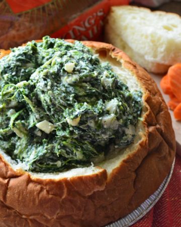 Close up of a bread bowl filled with spinach dip sitting in a metal tray.