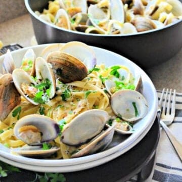 white bowl filled with clams and pasta with a skillet in the background.