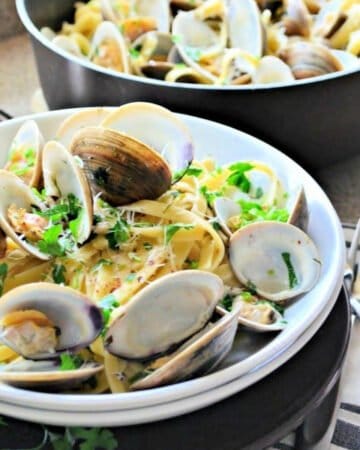 white bowl filled with clams and pasta with a skillet in the background.