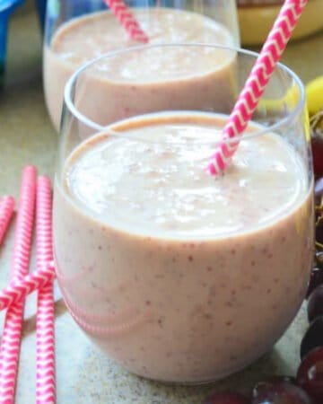 Two glasses of light pink smoothie with pink straws next to it.
