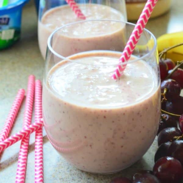 Two glasses of light pink smoothie with pink straws next to it.