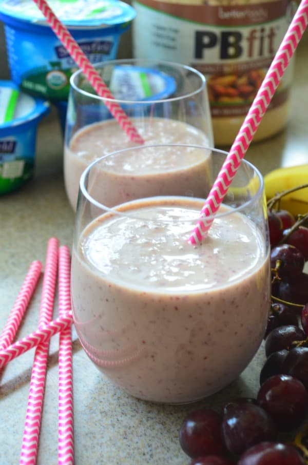Two glasses filled with pink smoothie, paper straws, and grapes. 