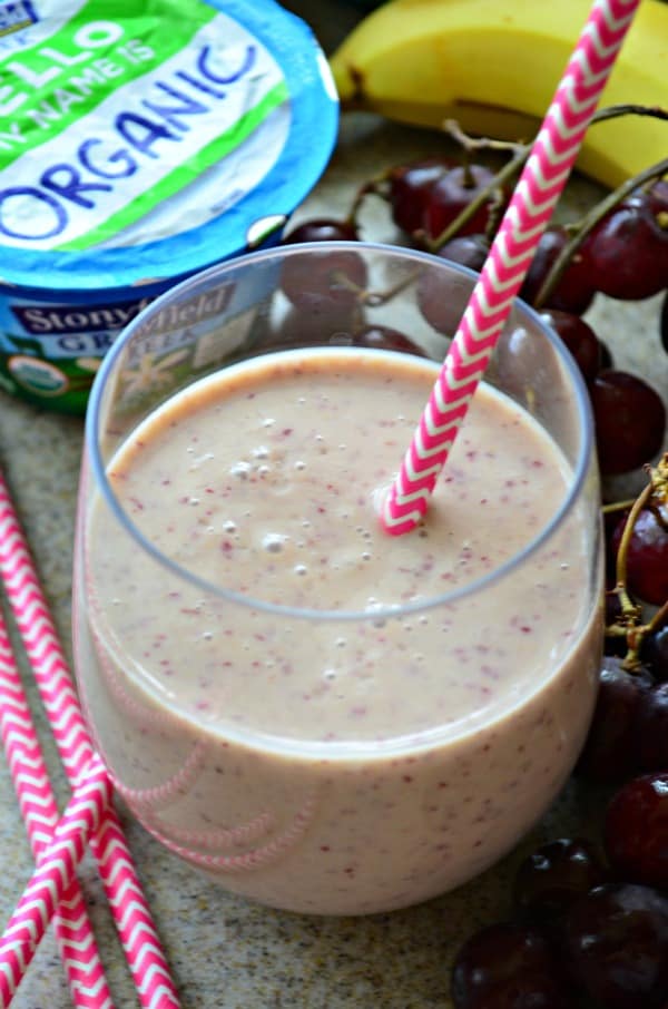 Close up of a glass filled with a pink smoothie, chevron pink straws and grapes.