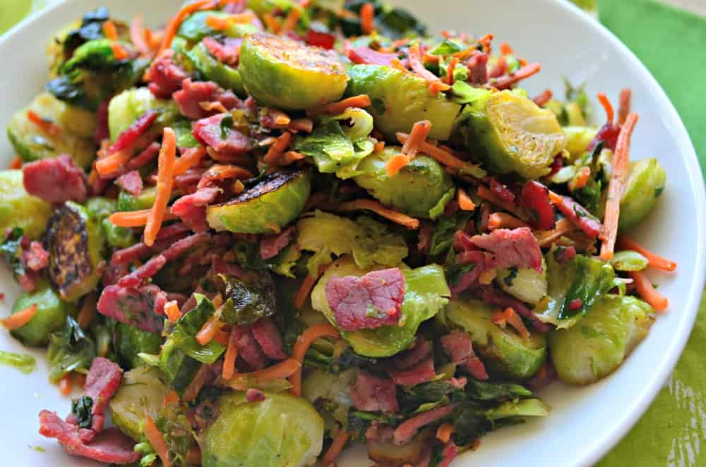 White bowl with brussel sprouts, shredded carrots, and corned beef.