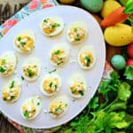 a white plate with multiple deviled eggs and cilantro on the side