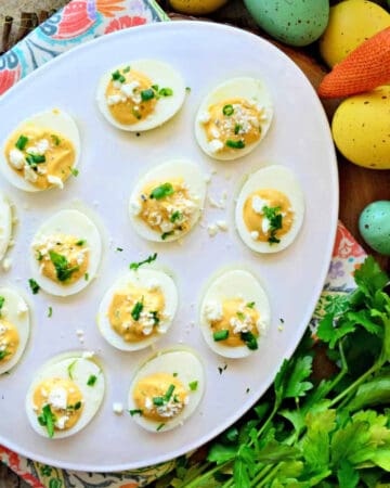 a white plate with multiple deviled eggs and cilantro on the side