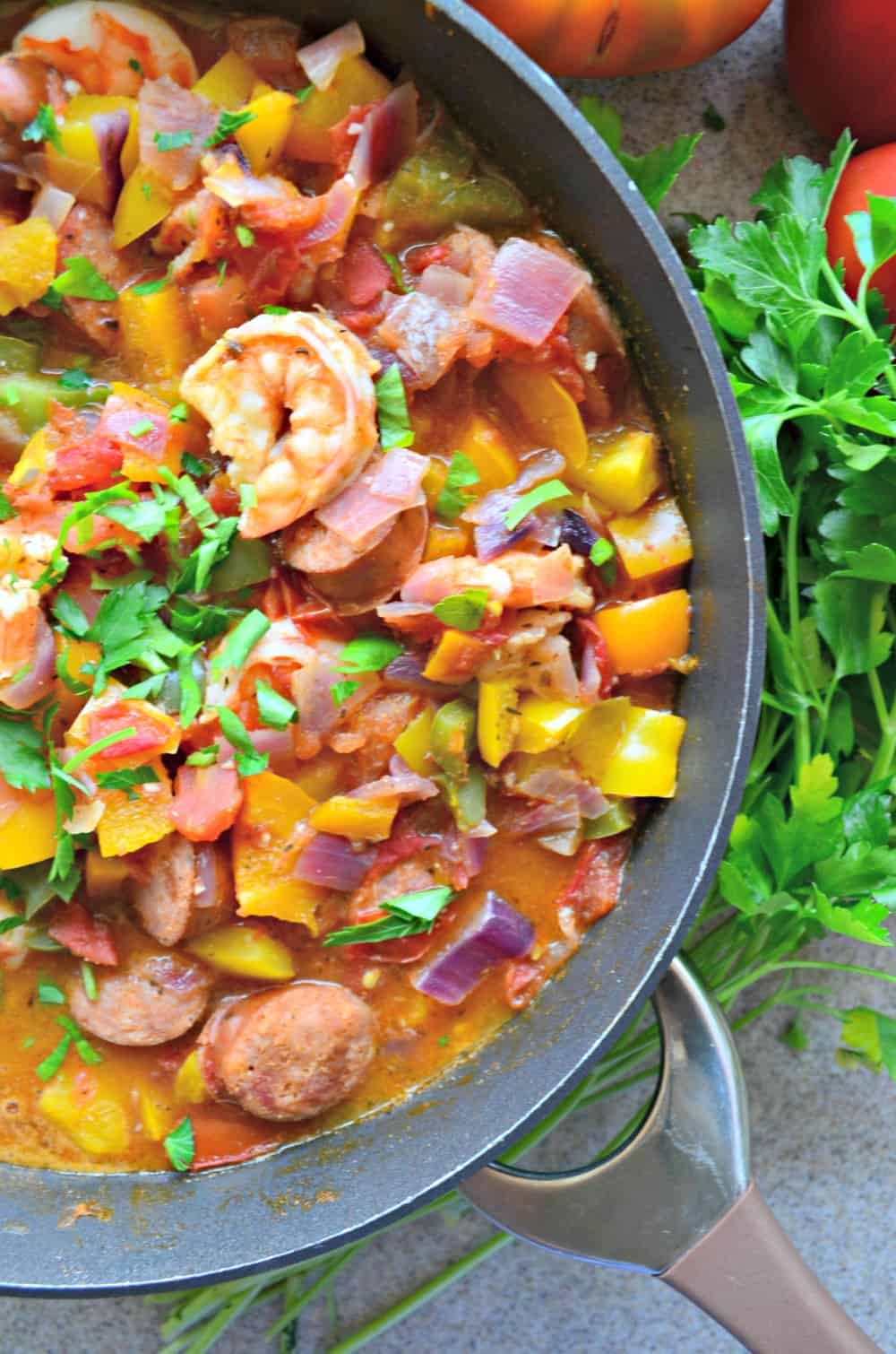 Top view of a skillet filled with red onion, bell peppers, sausage, and shrimp.