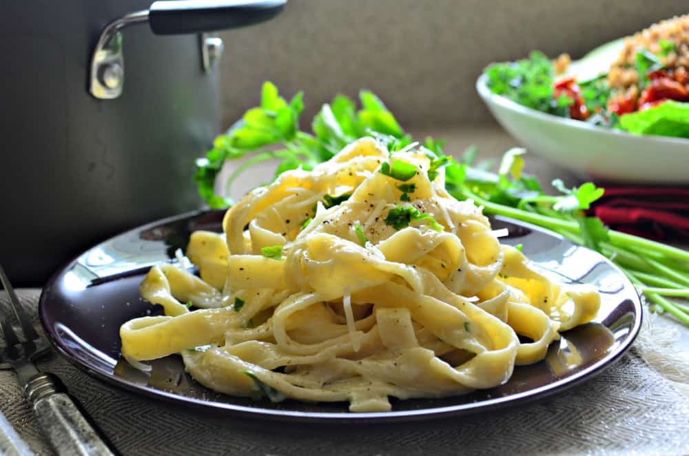 Fettuccine Alfredo Pasta on a purple plate garnished with Parmesan cheese, black pepper, and fresh parsley.