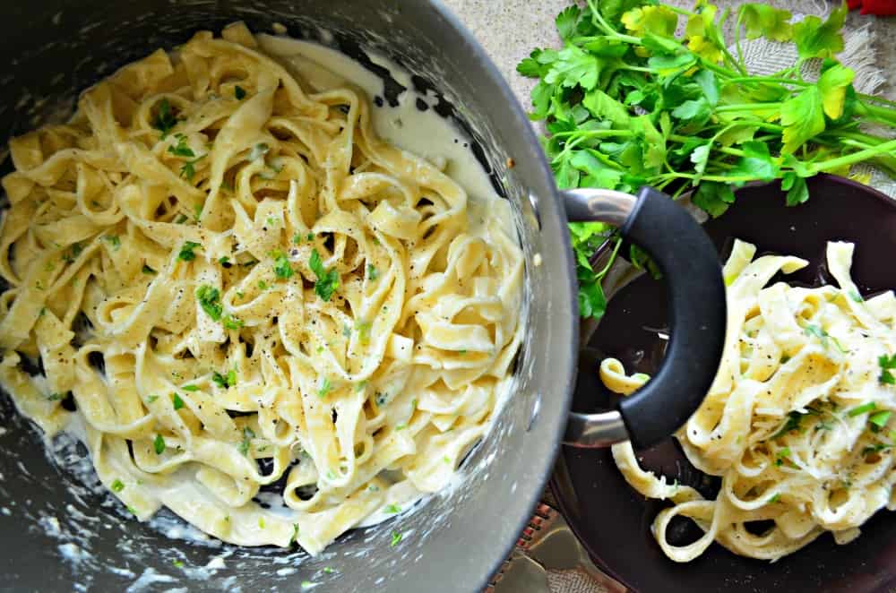 Top view of a big pot of Fettuccine Alfredo topped with fresh parsley and black pepper.