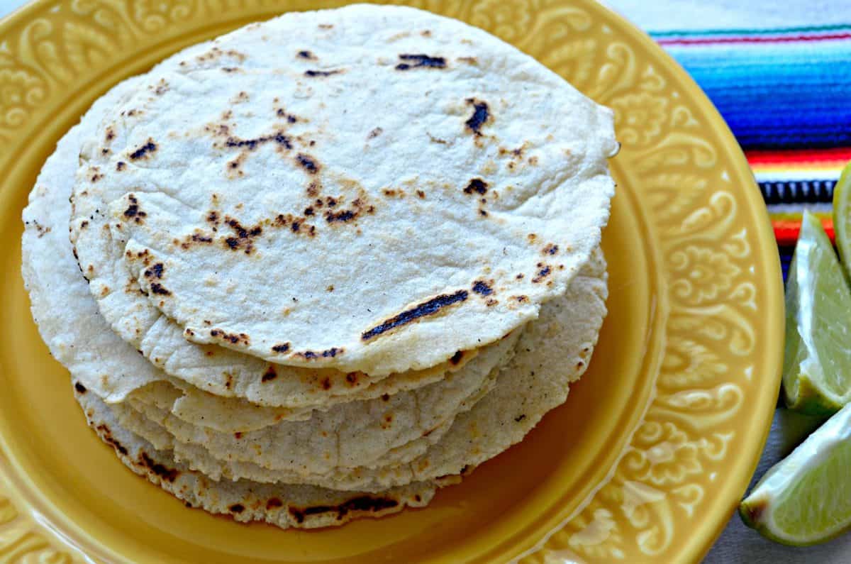 Yellow plate with a stack of tortillas with limes on the side. 