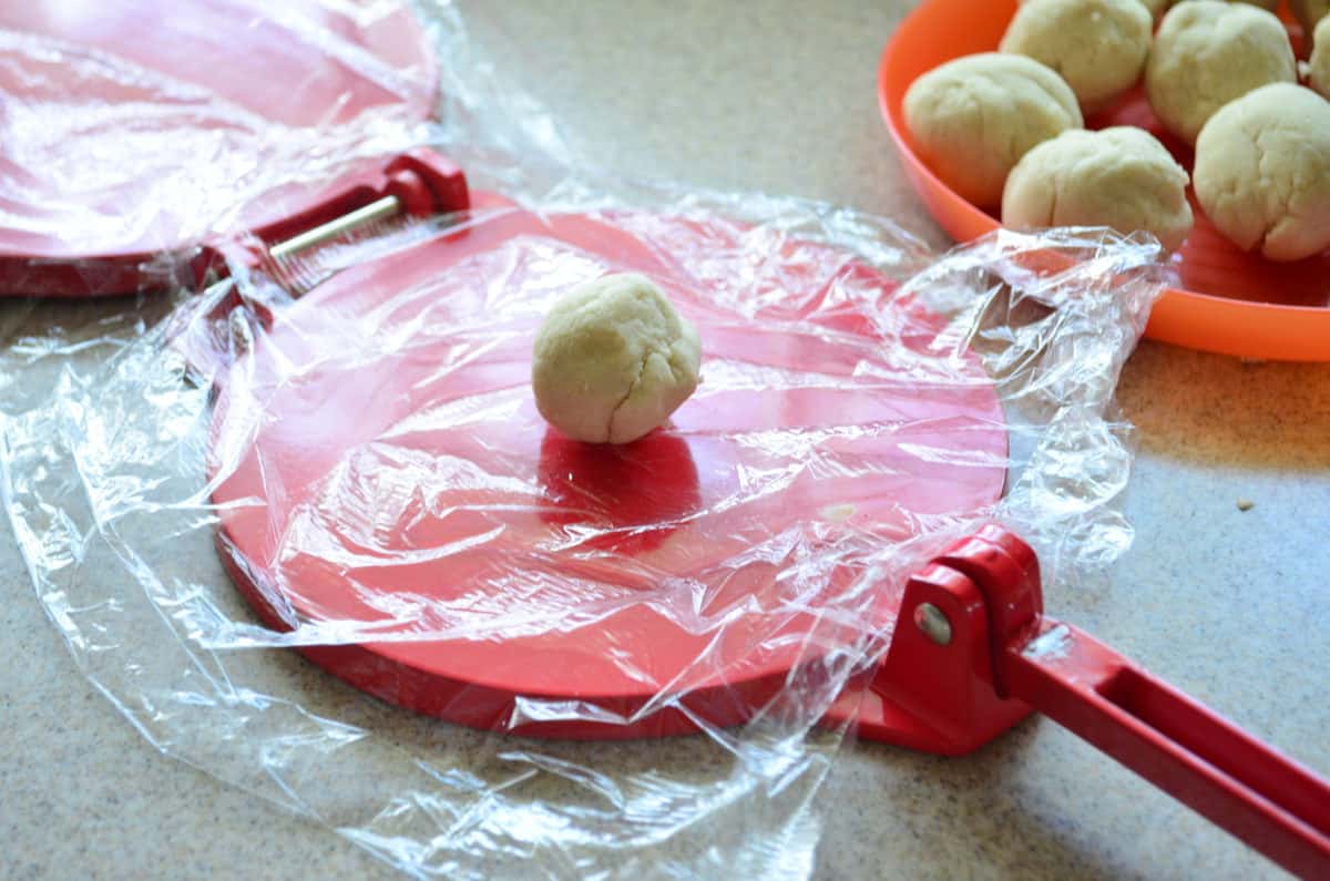 Red tortilla press, with plastic wrap on press with ball of dough in the middle.