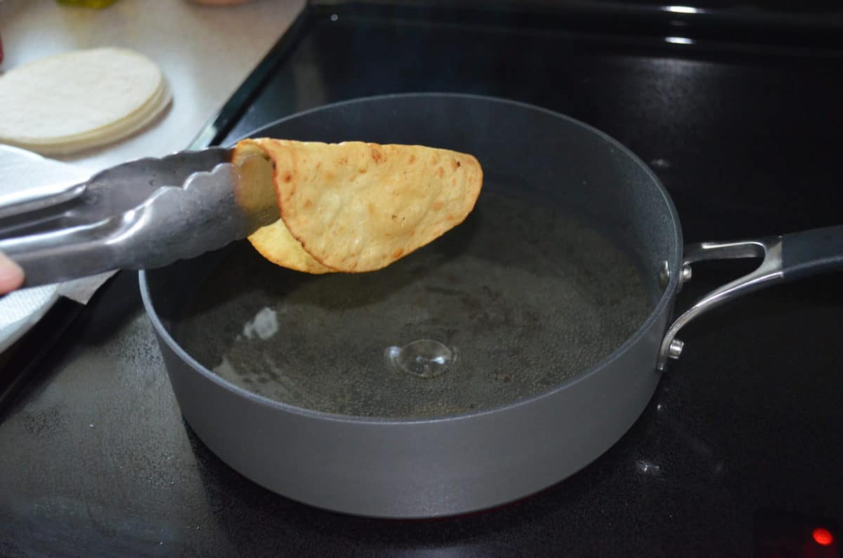 tongues holding soft tortilla over pan of hot oil prior to hardening shell.