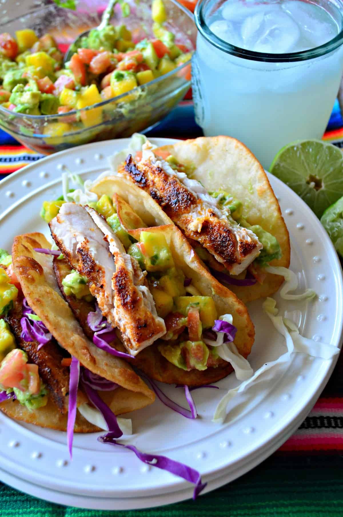 closeup Fish Tacos with Mango Avocado Salsa with a margarita and avocado mango salsa in the background. 