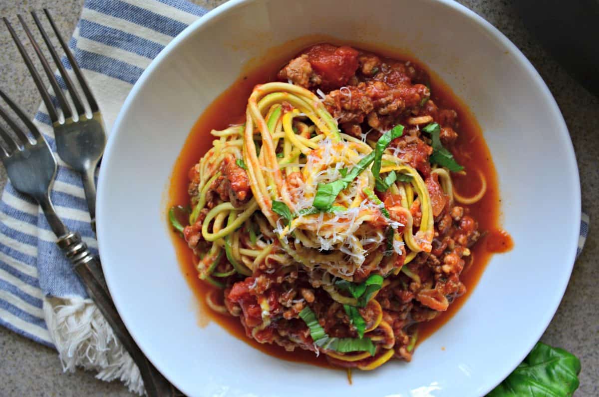 Top view of a white bowl filled with meat sauce and zucchini noodles on a dish towel.