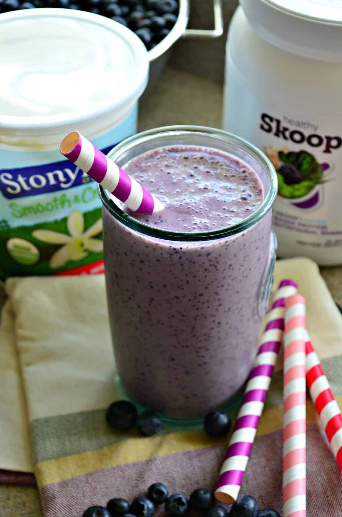 Tall glass filled with a blueberriy smoothie with protein powder and yogurt container in background.