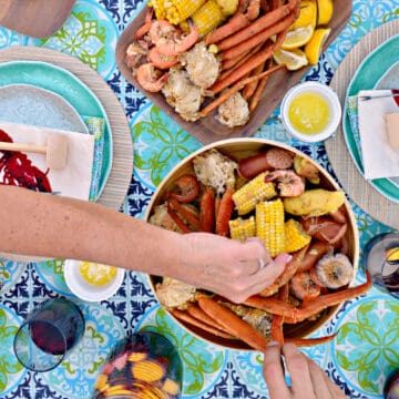 Female and man hand grabbing crab legs and corn in a seafood bowl.