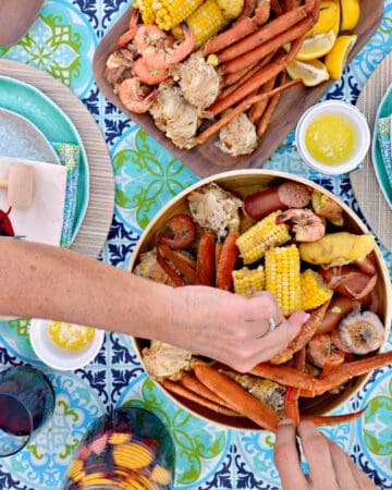 Female and man hand grabbing crab legs and corn in a seafood bowl.