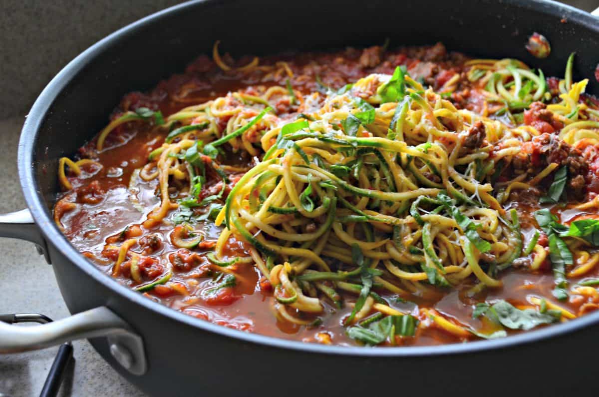 Black skillet filled with meat sauce, zucchini noodles, and cheese.