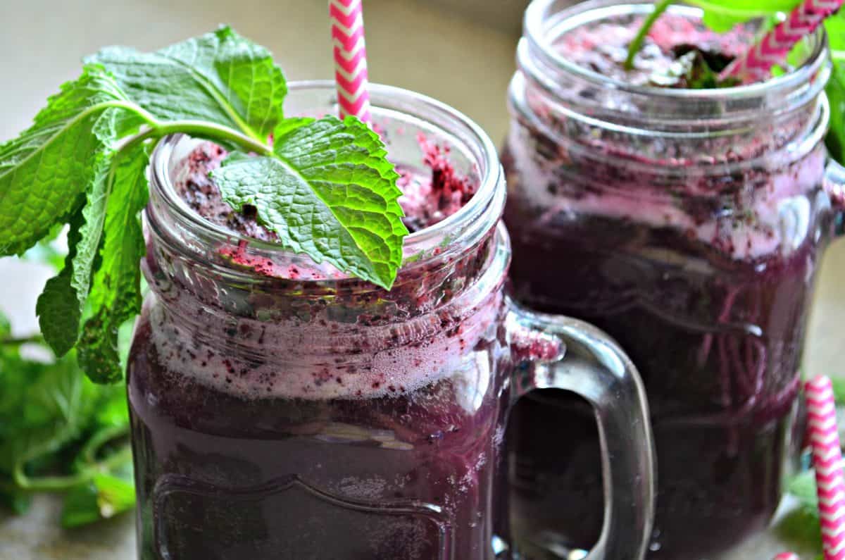 Two blueberry drinks with fresh mint and pink and white paper straws in glass.