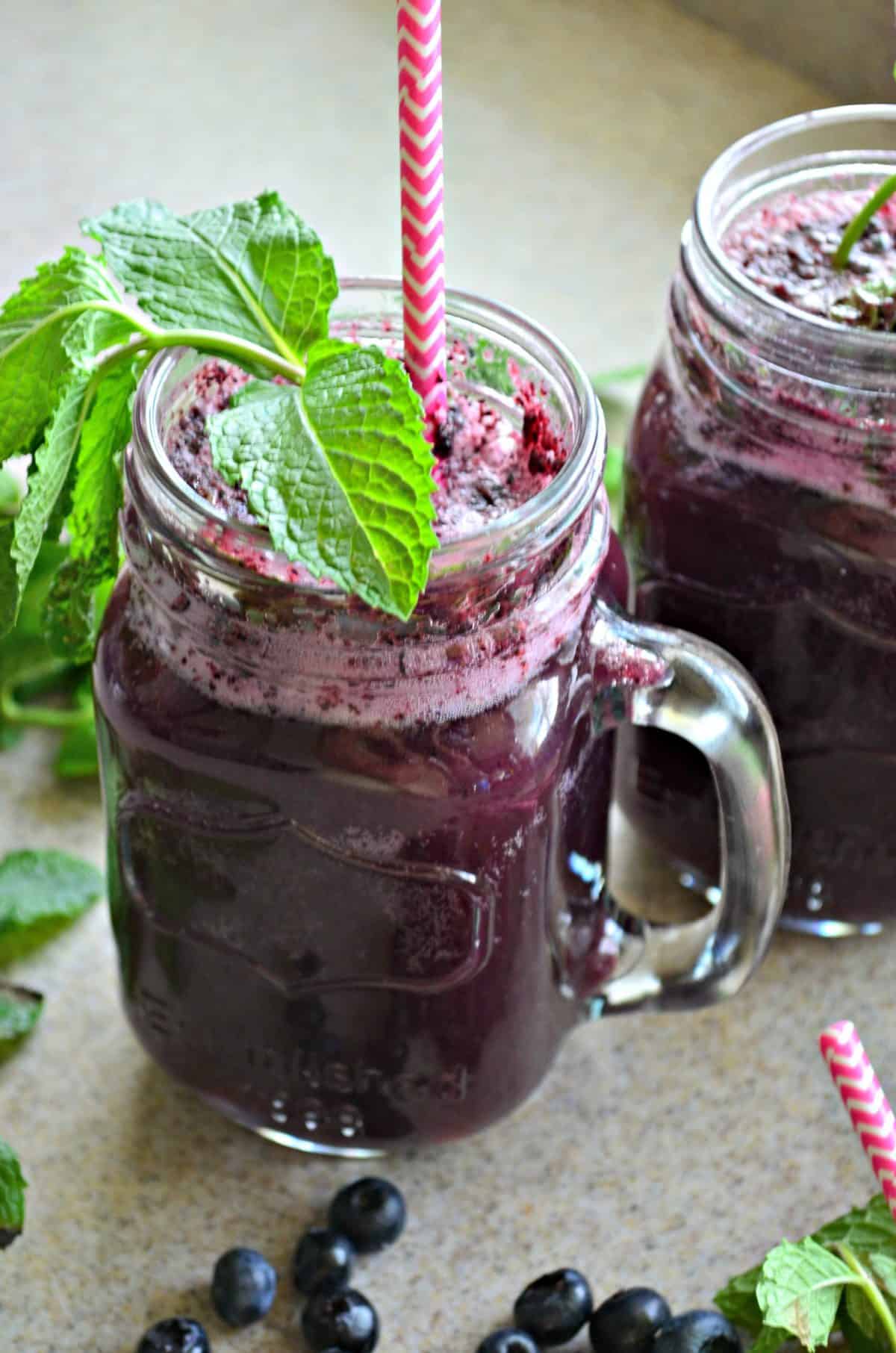 Up close of a blue looking drink with fresh mint in a mason jar style glass and a pink straw. 