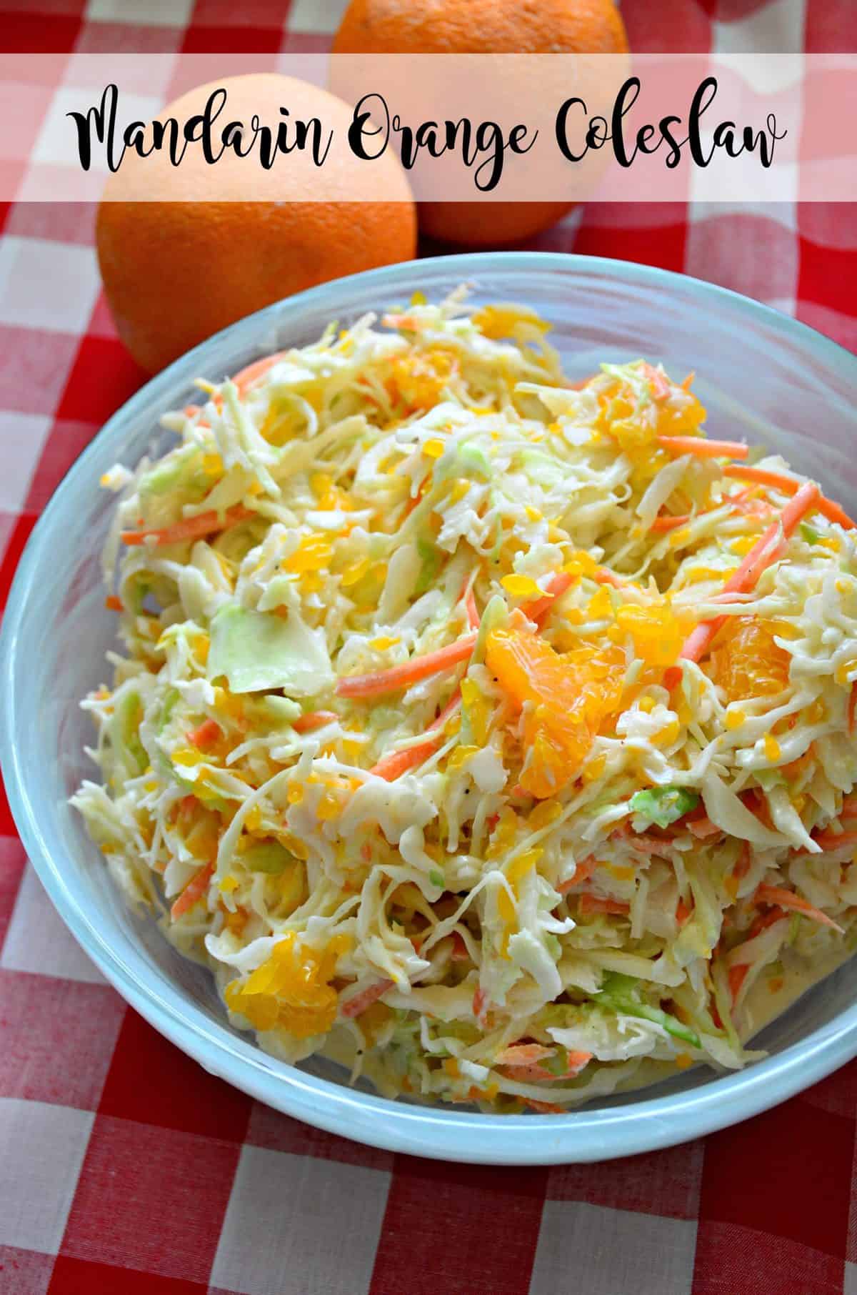Closeup of a blue bowl with coleslaw that has oranges in it on a red and white checkered cloth.