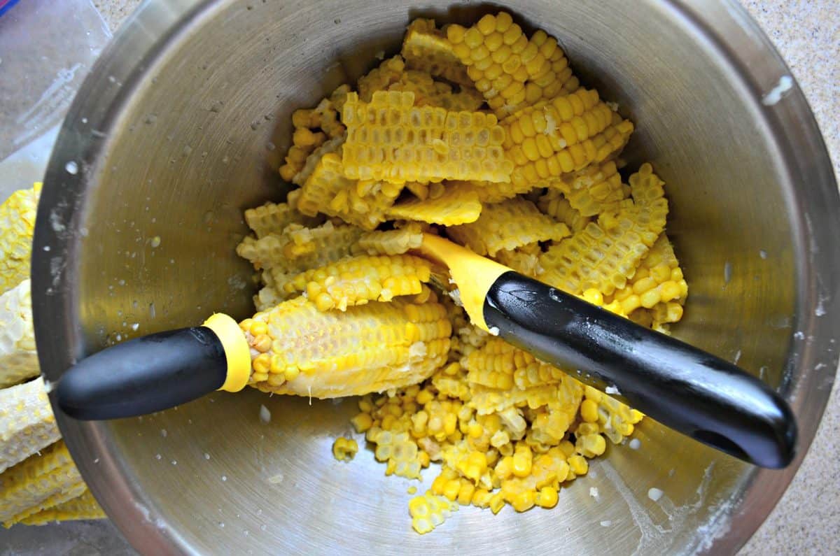 Top view of a silver bowl with corn kernels removed off a corn cob and a corn stripper in the bowl.